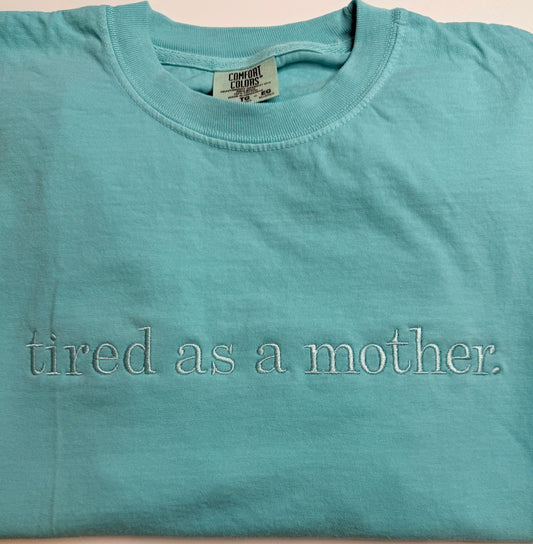 Teal t-shirt with 'tired as a mother' text on a beige background