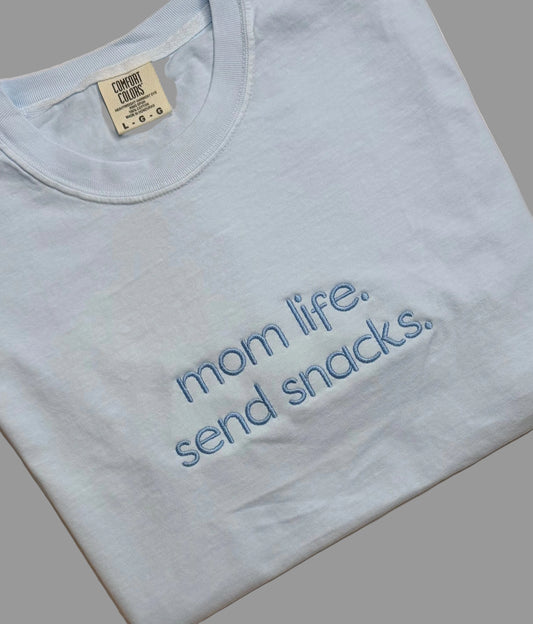 Light blue t-shirt with 'mom life. send snacks.' text on a gray background