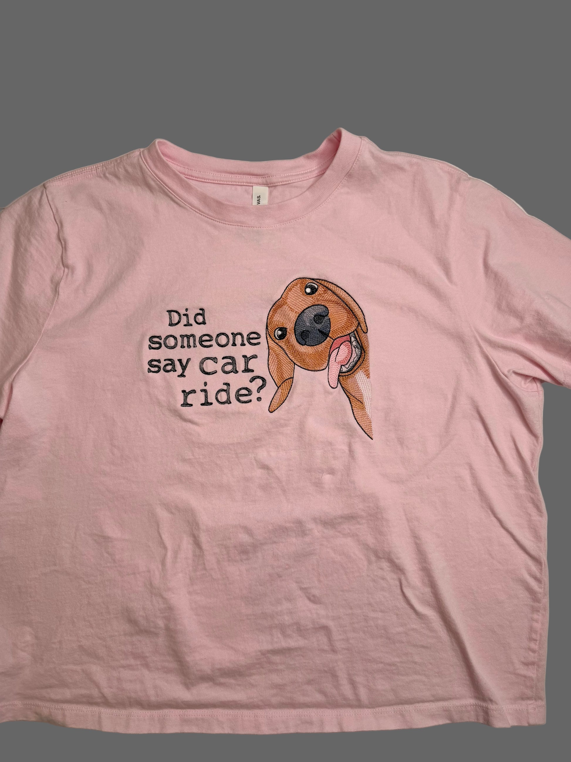 Pink t-shirt with a dog graphic and text on a plain background