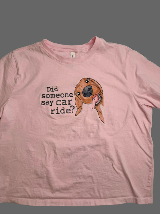 Pink t-shirt with a dog graphic and text on a plain background