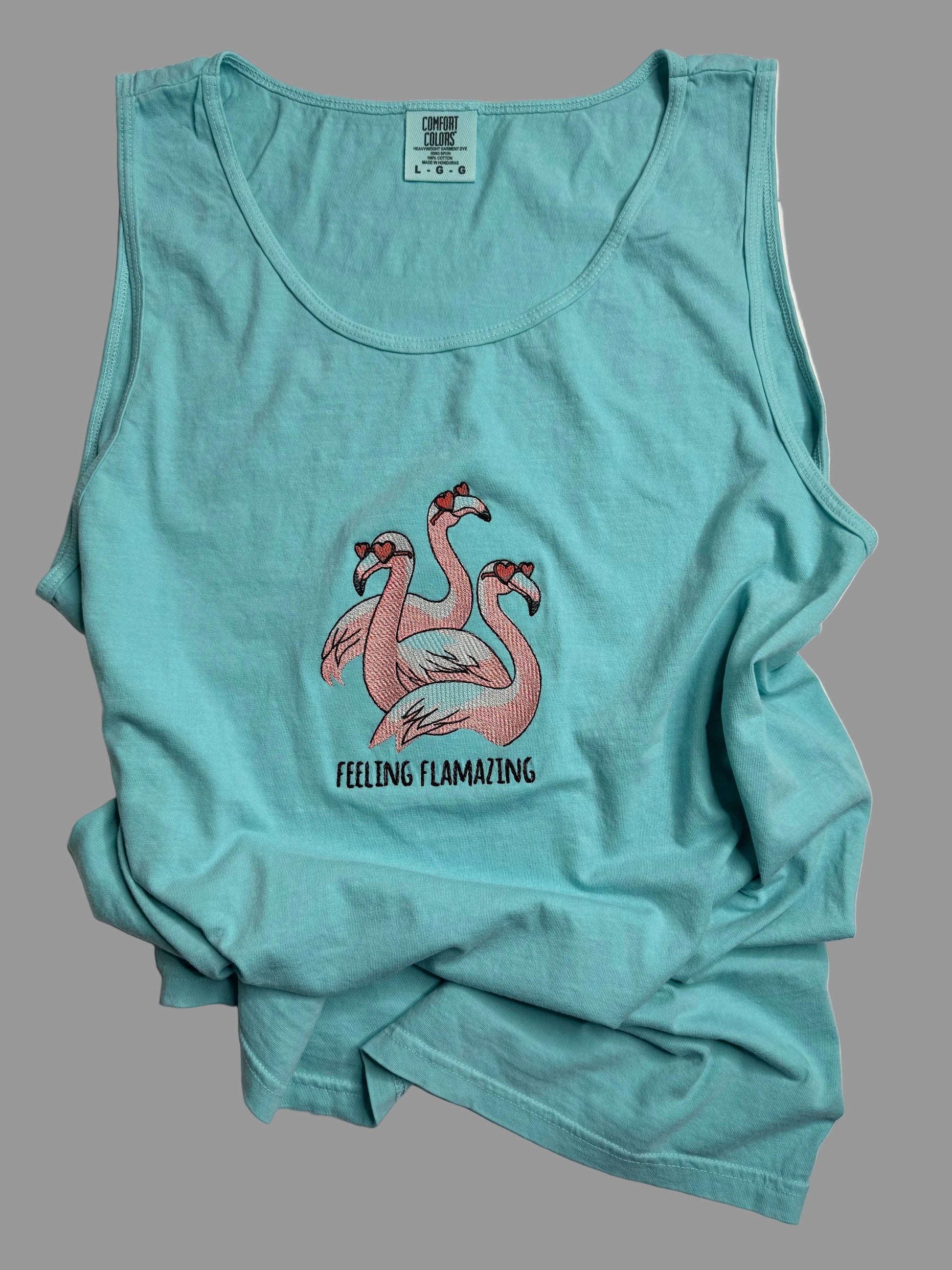 Teal tank top with flamingo design and 'Feeling Flamazing' text on a light gray background