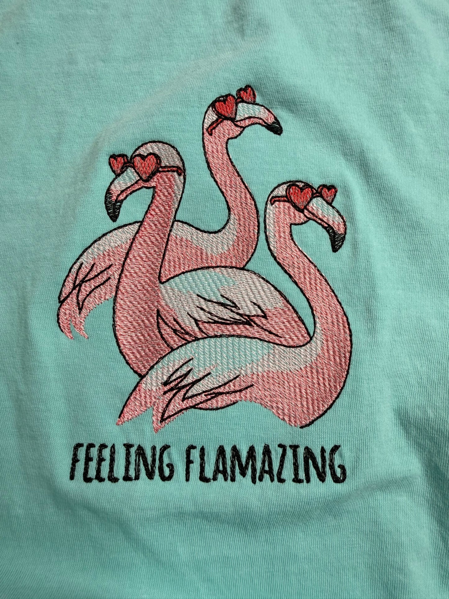 Embroidered flamingo design on a light mint fabric with 'Feeling Flamazing' text.