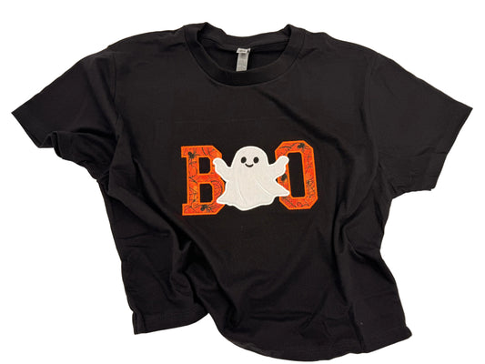 A black short-sleeve t-shirt laid flat on a white background, featuring a Halloween graphic on the front with the word 'BOO' in orange and a white ghost.