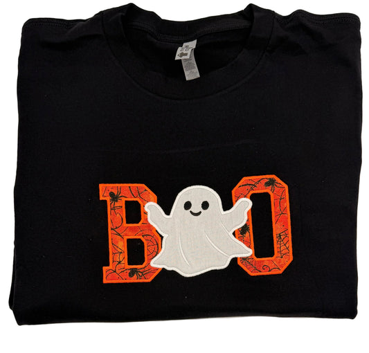 A folded black t-shirt featuring a 'BOO' graphic with orange spiderweb-patterned letters and a white ghost in the middle, displayed on a white background.