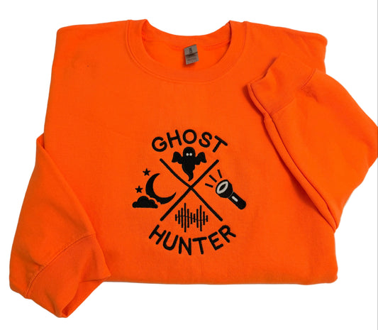 An orange crewneck sweatshirt with a black 'Ghost Hunter' graphic on the front, folded on a white surface.
